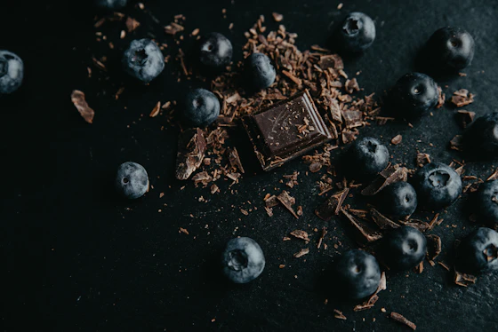 Quadrados de chocolate amargo ao lado de frutas vermelhas frescas sobre fundo escuro, iluminação cinematográfica