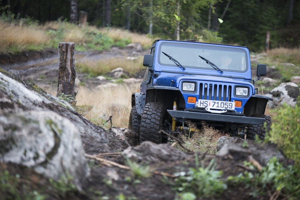 a blue jeep driving through a forest filled with rocks