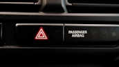 A close-up view of a car dashboard displaying an emergency hazard button with a red triangle symbol next to a passenger airbag indicator. The passenger airbag section has an icon indicating its on and off status.