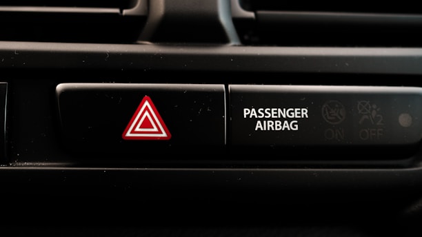 A close-up view of a car dashboard displaying an emergency hazard button with a red triangle symbol next to a passenger airbag indicator. The passenger airbag section has an icon indicating its on and off status.