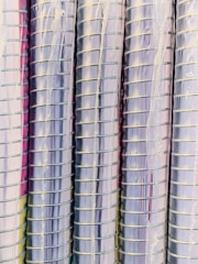 Rows of metallic, cylindrical tubes stacked vertically with a reflective surface that gives off a shiny appearance. The tubes are wrapped in a thin, translucent plastic cover.