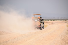 A vehicle driving along a dirt road near open land