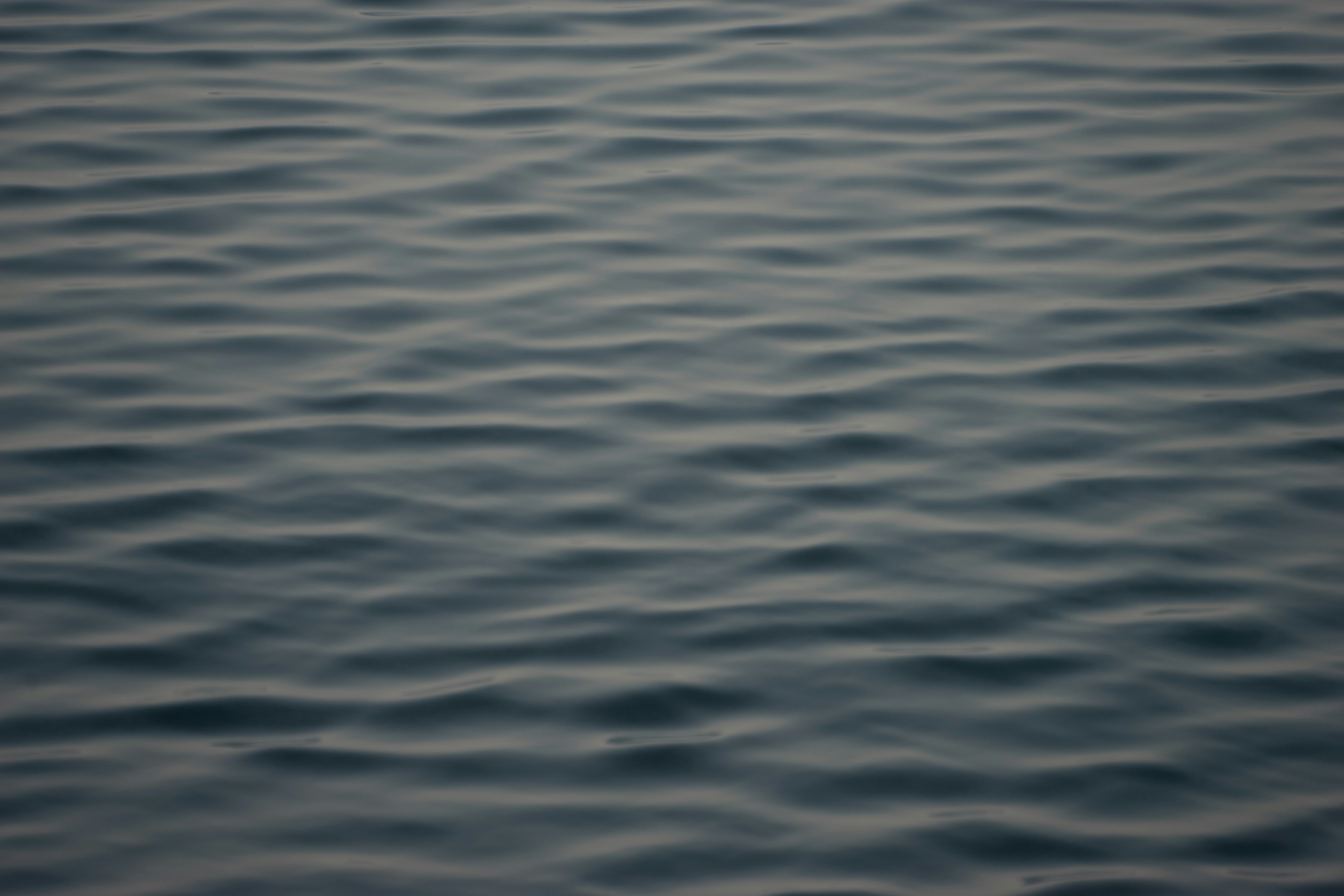 Still water surface with single ripple expanding outward, minimal and meditative, dark background