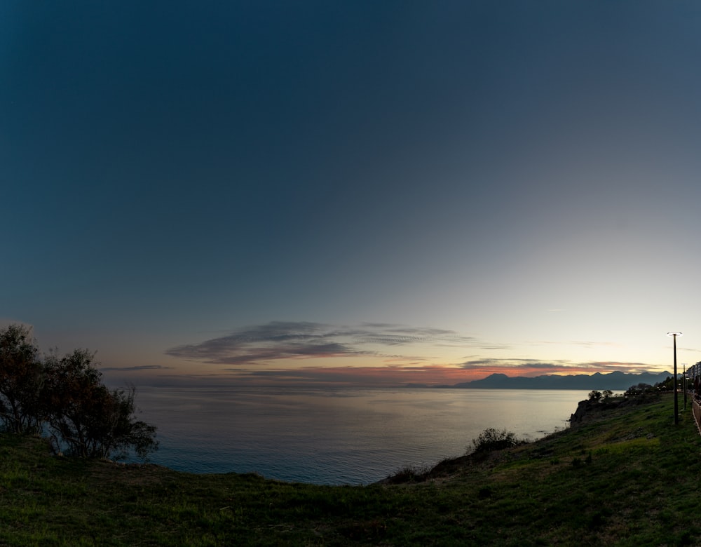 the sun is setting over the ocean on a hill