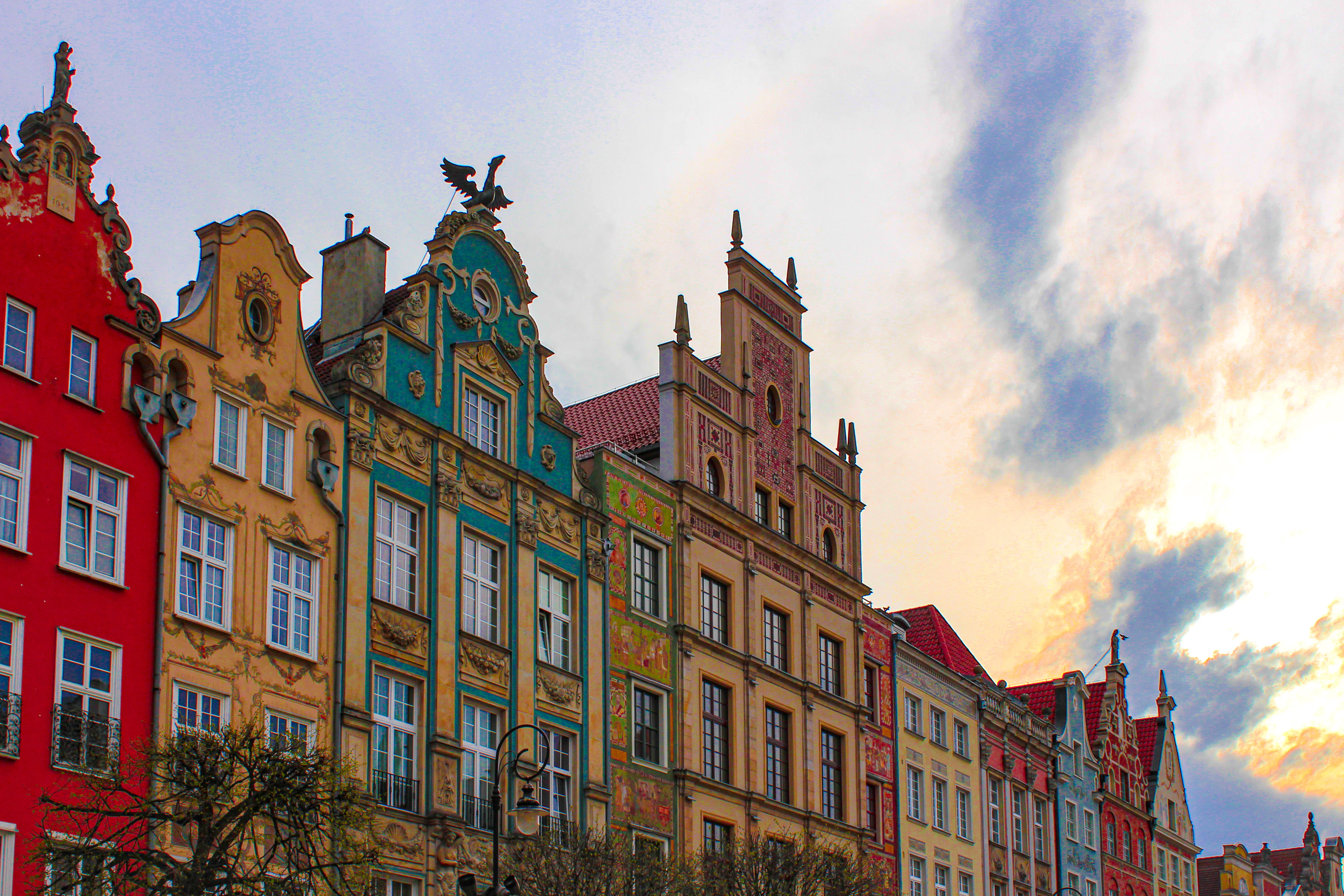 A close-up of Gdańsk's ornately gabled, brightly painted townhouse facades on the Long Market, glowing under a dusk sky.
