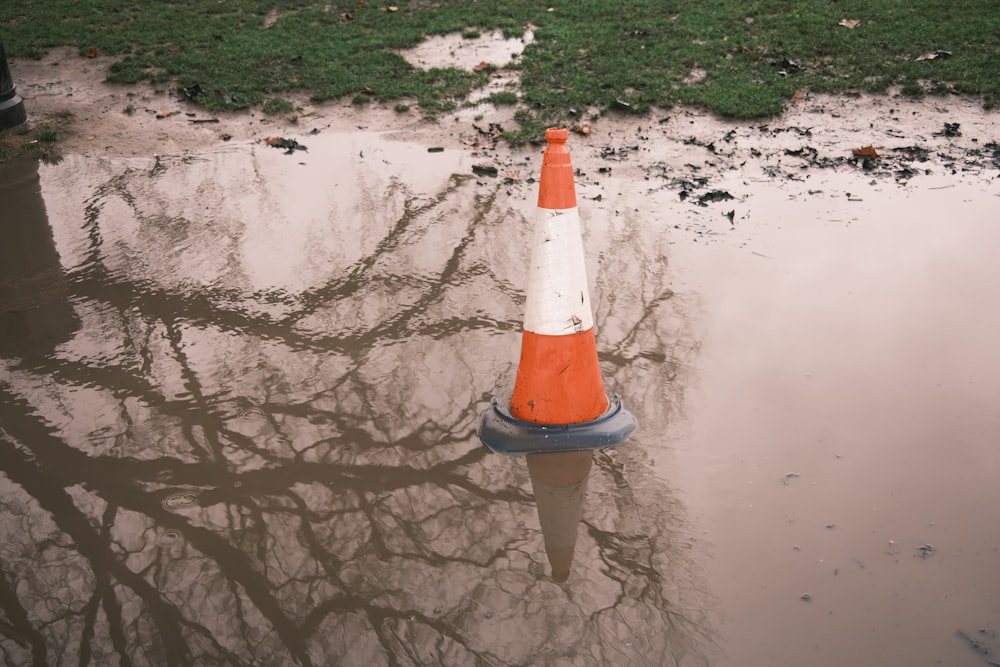 an orange and white cone sitting in a puddle of water
