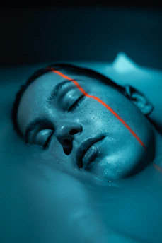 Close-up of a person's face with closed eyes in teal light, crossed by a thin orange line