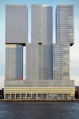 A modern architectural structure comprised of interconnected rectangular towers featuring grid-like patterns on their surfaces. The building is situated by a water body and includes signage indicating 'AQUA ASIA' at the lower level.