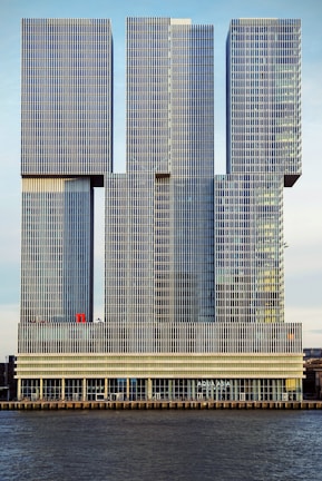 A modern architectural structure comprised of interconnected rectangular towers featuring grid-like patterns on their surfaces. The building is situated by a water body and includes signage indicating 'AQUA ASIA' at the lower level.