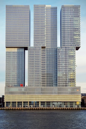 A modern architectural structure comprised of interconnected rectangular towers featuring grid-like patterns on their surfaces. The building is situated by a water body and includes signage indicating 'AQUA ASIA' at the lower level.
