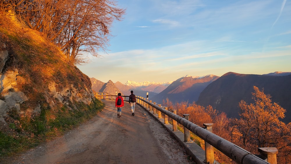 a person walking down a dirt road next to a mountain