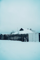 A classic white picket fence surrounding a snowy yard under a clear blue Alaskan sky.