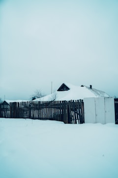 A classic white picket fence surrounding a snowy yard under a clear blue Alaskan sky.