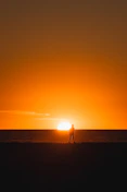 a person walking on a beach at sunset