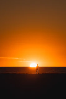 a person walking on a beach at sunset