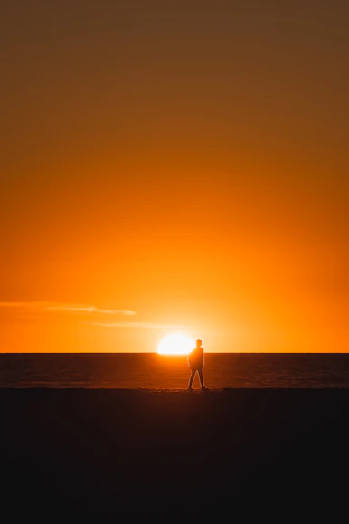 a person walking on a beach at sunset