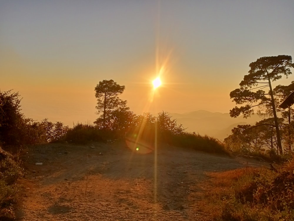 the sun is setting over a hill with trees