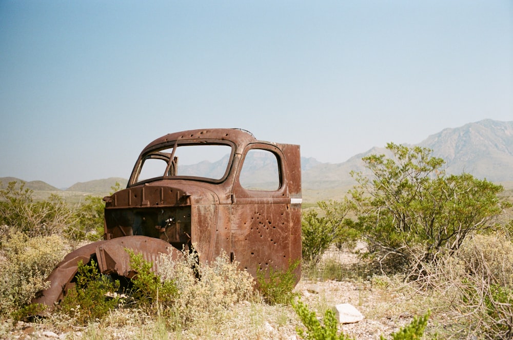 an old rusted out truck in a field with mountains in the background