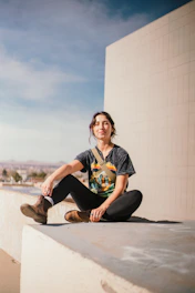 A relaxed young person wearing a sleek graphic t-shirt, lounging on a cloud-shaped chair with a city skyline in the background.