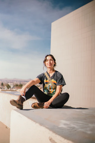 A relaxed young person wearing a sleek graphic t-shirt, lounging on a cloud-shaped chair with a city skyline in the background.