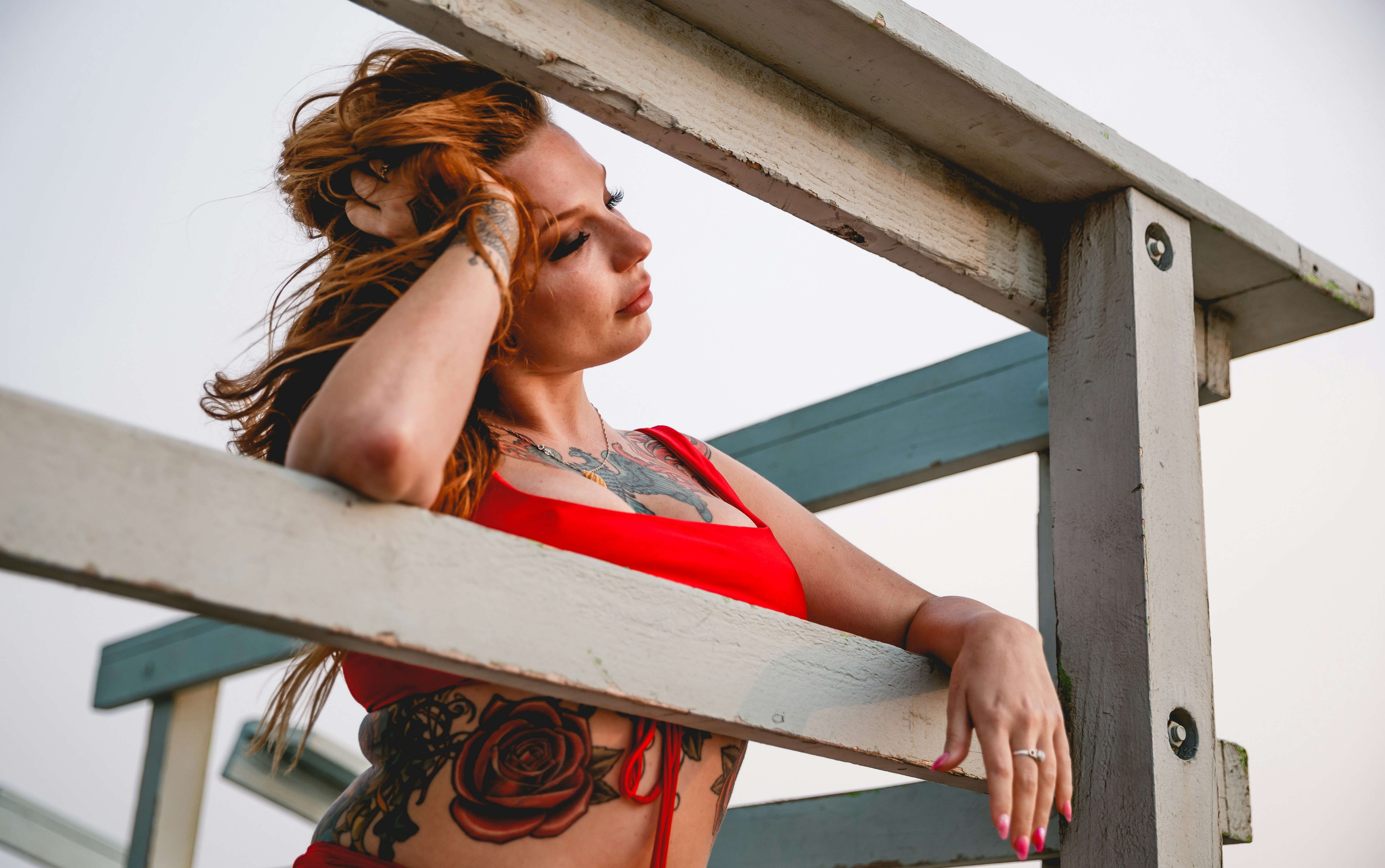a woman in a red top leaning on a wooden fence