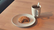 A warm cup of coffee next to a plate of assorted cookies on a wooden table.