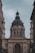 A large, ornate building with classical architecture, featuring a prominent, dark-colored dome. The facade is adorned with columns and detailed sculptures, including a depiction of religious scenes above the entrance. The inscription 'EGO SUM VIA VERITAS ET VITA' is visible across the archway.