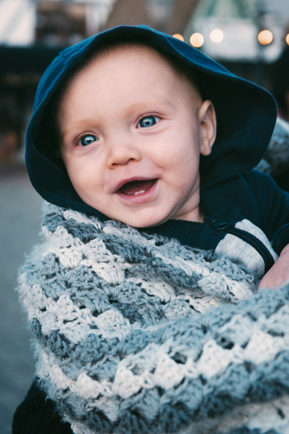 a smiling baby wearing a gray and white crochet scarf