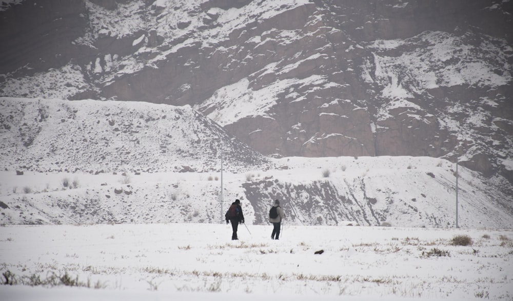 a couple of people walking across a snow covered field