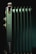 A close-up view of a metallic, green radiator with multiple vertical fins. The lighting highlights the metallic components and edges, creating a contrast with the dark background.