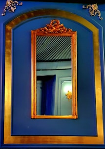 An elegant mirror with a sleek navy blue frame reflecting a cozy living room corner.