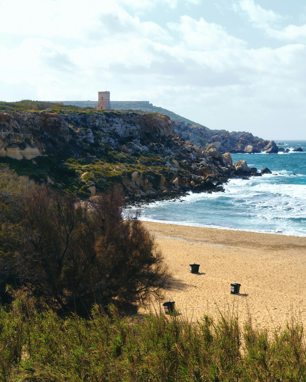 a sandy beach next to the ocean with a tower in the background