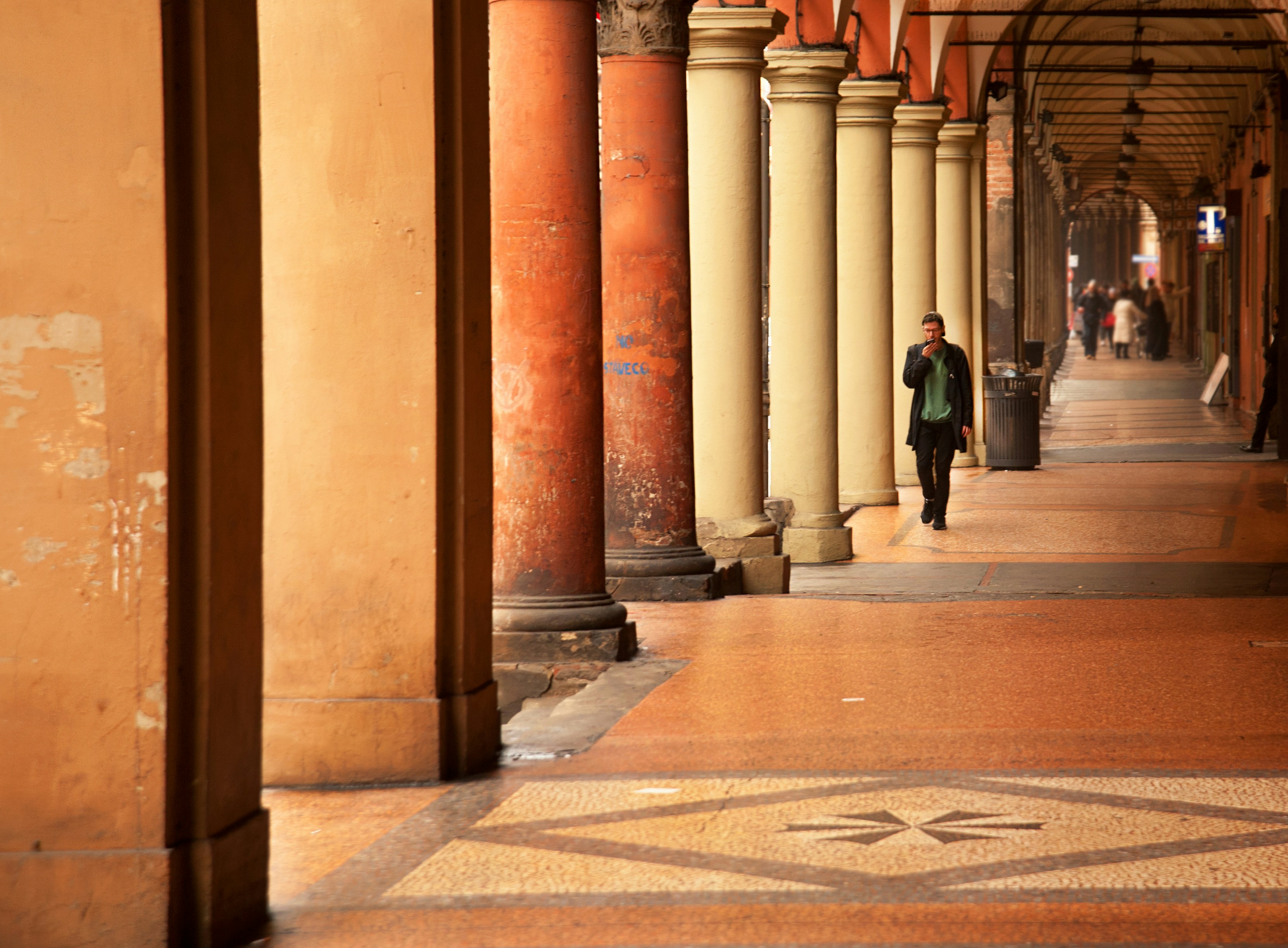 a man walking down a sidewalk next to tall pillars