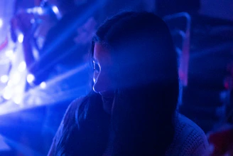 A dark, cinematic close-up of a person whispering secrets in a shadowy room with neon blue accents.