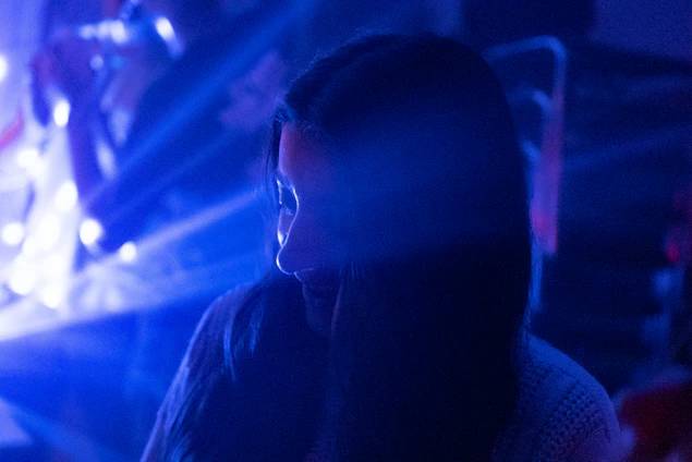 A dark, cinematic close-up of a person whispering secrets in a shadowy room with neon blue accents.