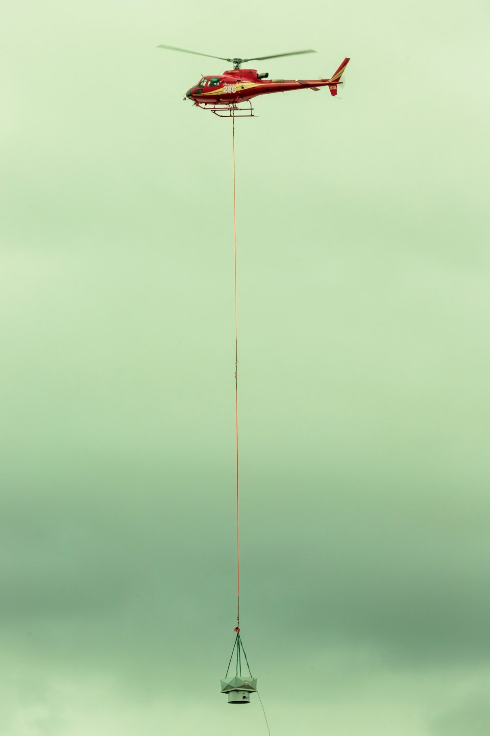 a helicopter being lowered by a crane on a cloudy day