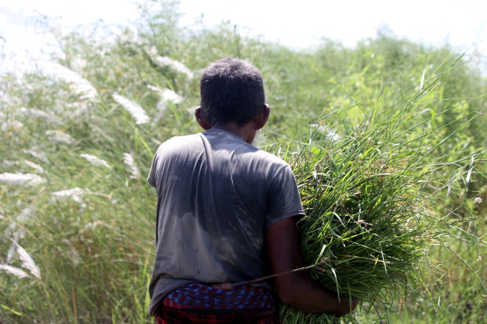 a man carrying a bundle of grass in a field