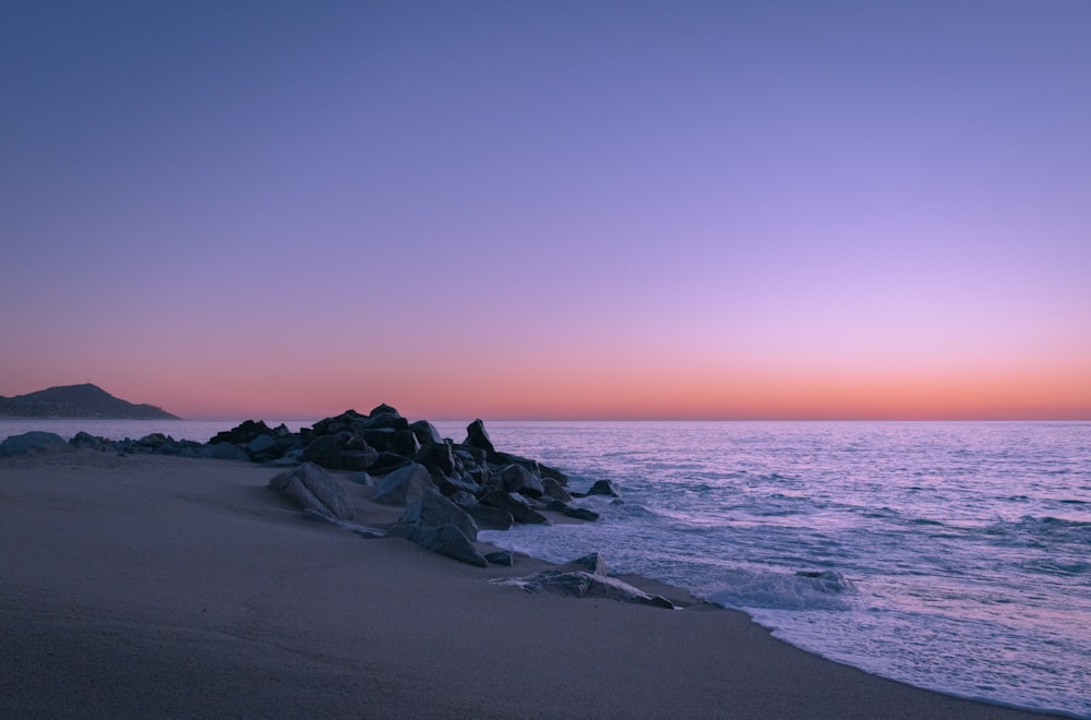 uma praia ao pôr do sol com rochas em primeiro plano