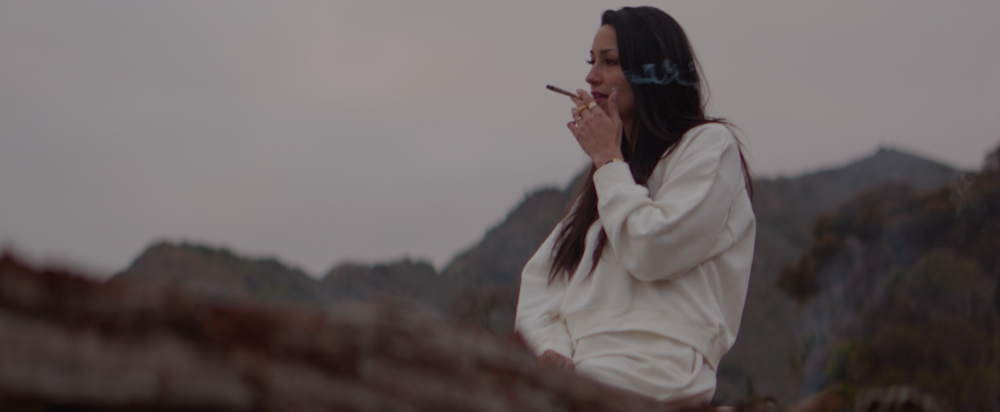 a woman smoking a cigarette in front of a mountain