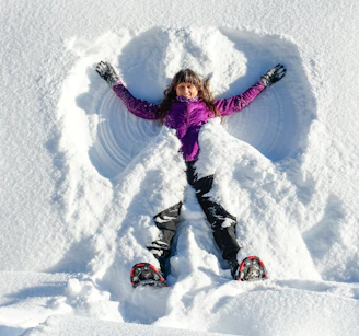 a young girl in a purple jacket standing in the snow
