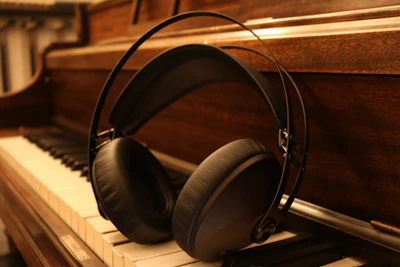 Close-up of headphones resting on a piano under soft shadows.