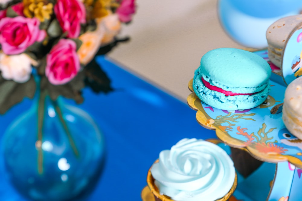 a blue table topped with cupcakes and a vase of flowers