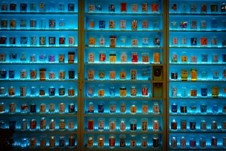 A well-organized display of various canned drinks, each uniquely decorated and illuminated by vibrant blue lighting. Shelves are filled with an array of colorful cans, featuring different designs and labels, potentially showcasing a collection of beverages.