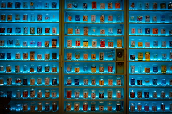 A well-organized display of various canned drinks, each uniquely decorated and illuminated by vibrant blue lighting. Shelves are filled with an array of colorful cans, featuring different designs and labels, potentially showcasing a collection of beverages.