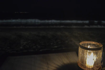 A serene seaside scene at dusk with a lit candle casting warm light on a stone ledge overlooking the crystalline sea.