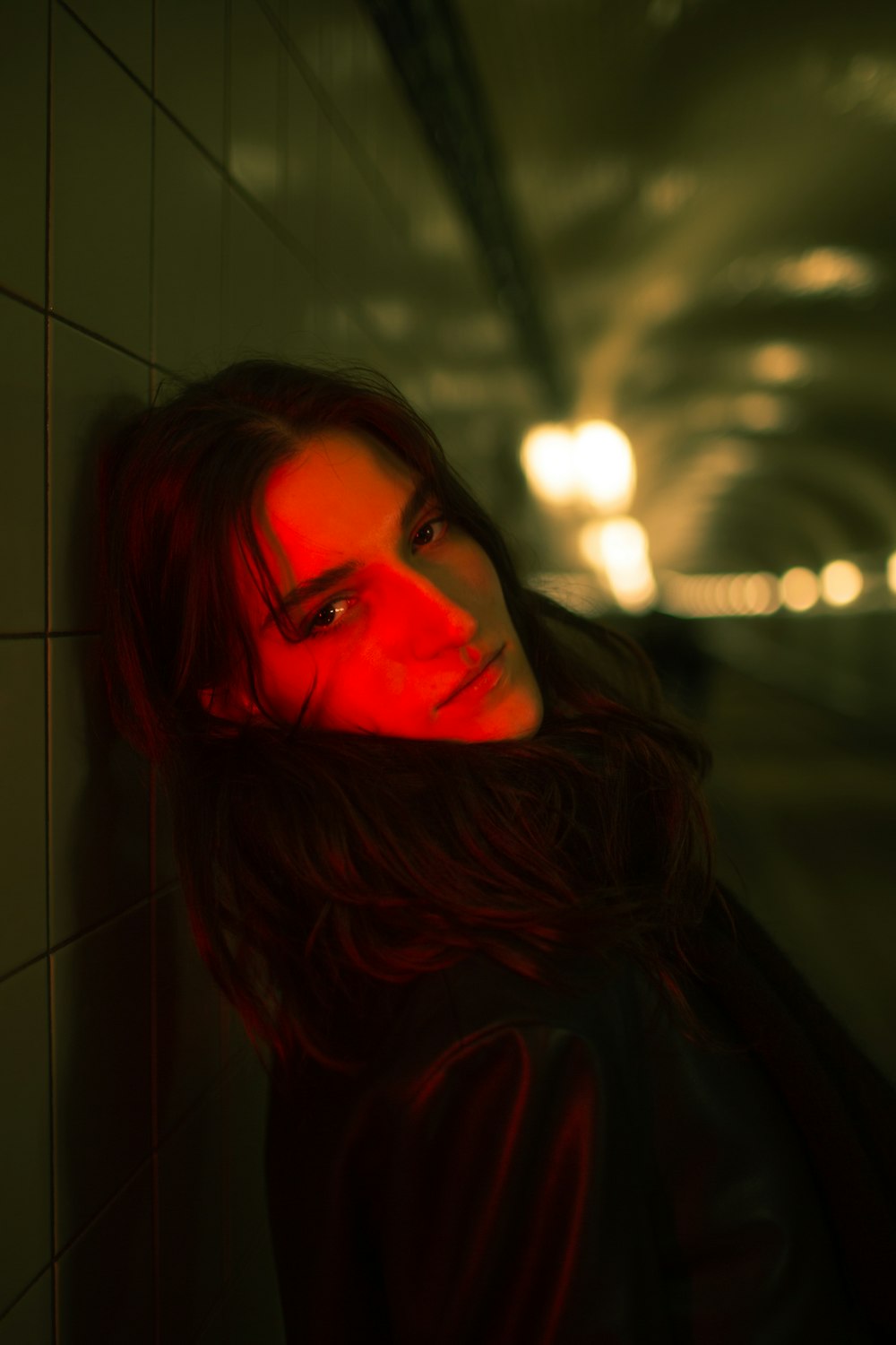 a woman leaning against a wall with a red light on her face