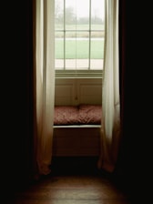 Cozy seating area by a window with gentle morning light filtering through sheer curtains.
