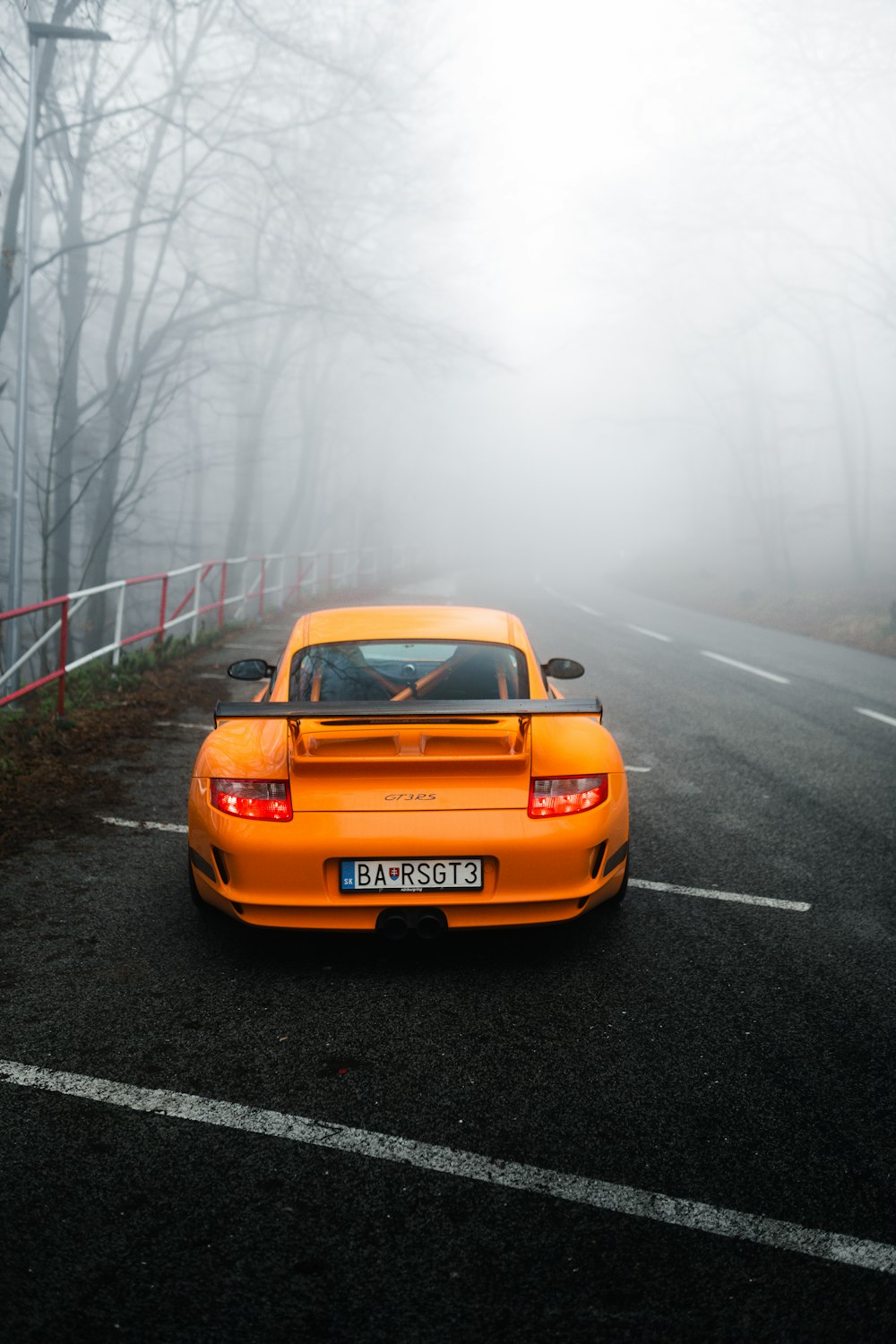 an orange sports car driving down a foggy road