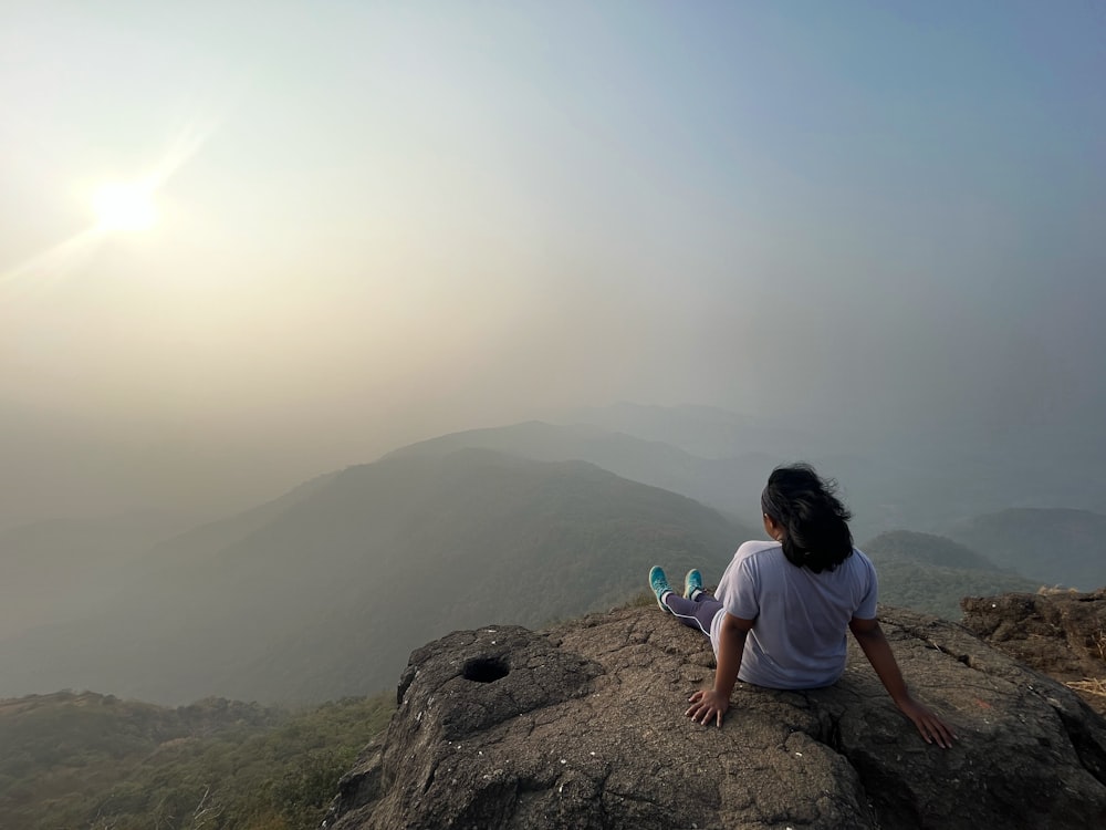 a woman sitting on top of a large rock