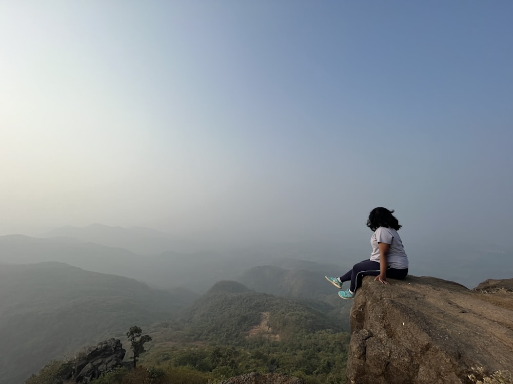 a woman sitting on top of a cliff overlooking a valley
